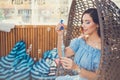 A young woman with bright makeup is sitting in a summer outdoor cafe in a hanging chair and blowing soap bubbles Royalty Free Stock Photo