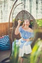 A young woman with bright makeup is sitting in a summer outdoor cafe in a hanging chair and blowing soap bubbles Royalty Free Stock Photo