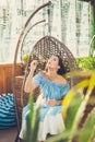 A young woman with bright makeup is sitting in a summer outdoor cafe in a hanging chair and blowing soap bubbles Royalty Free Stock Photo