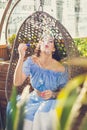 A young woman with bright makeup is sitting in a summer outdoor cafe in a hanging chair and blowing soap bubbles Royalty Free Stock Photo