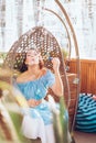 A young woman with bright makeup is sitting in a summer outdoor cafe in a hanging chair and blowing soap bubbles Royalty Free Stock Photo