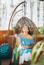 A young woman with bright makeup is sitting in a summer outdoor cafe in a hanging chair and blowing soap bubbles Royalty Free Stock Photo