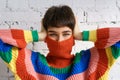 A young woman in a bright multicolored rainbow sweater hides her face and covers her ears with her hands Royalty Free Stock Photo