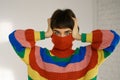 Young woman in a bright multicolored rainbow sweater hides her face and covers her ears with her hands. Royalty Free Stock Photo