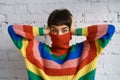 Young woman in a bright multicolored rainbow sweater hides her face and covers her ears with her hands. Royalty Free Stock Photo