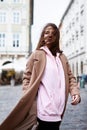 Young woman in brown coat and pink hoody posing on the street