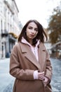 Young woman in brown coat and pink hoody posing on the street