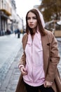 Young woman in brown coat and pink hoody posing on the street