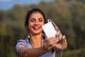 Selfie-taking woman, white phone, wired earphones, park Royalty Free Stock Photo