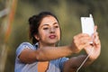 Selfie-taking woman, white phone, wired earphones, park Royalty Free Stock Photo