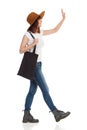 Young Woman In Brown Hat Is Walking With Black Bag On Her Shoulder And Waving Hand Royalty Free Stock Photo