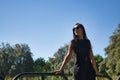 Young woman, brunette, slender, dressed in black and wearing sunglasses, leaning on a railing in a park. Concept beauty, fashion, Royalty Free Stock Photo