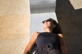 Young woman, brunette, slender, dressed in black and wearing sunglasses, lying on a bench receiving the sun's rays relaxed. Royalty Free Stock Photo