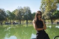 Young woman, brunette, slender, dressed in black and wearing sunglasses, with one hand on her chin, leaning on a railing next to a Royalty Free Stock Photo