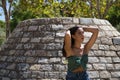 Young woman, brunette, slender, dressed in green t-shirt and jeans, leaning against a stone wall, hands in her hair relaxed. Royalty Free Stock Photo