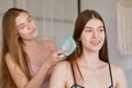 Young woman brushing hair of female friend, friendship and femininity concept