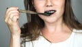 Young woman brushing her teeth with a black tooth paste with active charcoal, and black tooth brush on white background for Teeth
