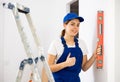 Satisfied young woman builder checking vertical of walls with level