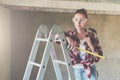 A young woman builder, dressed in a plaid shirt and construction glasses, stands on a stepladder and holds roulette Royalty Free Stock Photo