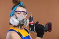 young woman builder in a protective mask and glasses stands in her hands in a screwdriver, a construction tool, a studio