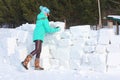 Young woman builds snow castle wall of snow blocks. Winter vacation. Winter and new year holidays