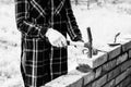Young woman builds a wall of bricks, lays a brick on a cement-sand mortar, tapping a brick with a hammer