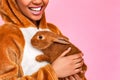 Freestyle. Young woman in kigurumi standing isolated on pink with rabbit close laughing cheerful close-up