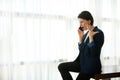 Young woman in a business casual suit sits at the edge of a table by the window of a hotel room and argues, gesturing with her Royalty Free Stock Photo