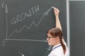 Young woman business coach in a white blouse and glasses at the chalkboard in the office draws a profit graph