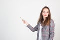 young woman in business formal clothes poses against a white wall and points at something