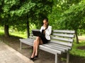 Young woman in a business suit drinks coffee and works on a laptop while sitting on a bench in the park, side view. Lonely adult Royalty Free Stock Photo