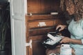 Young woman busy in restoring old wooden cabinet furniture alone at home painting with white color and roller brush. Renovating Royalty Free Stock Photo