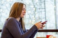 Young woman at cafe drinking coffee and using smartphone and wifi, connects to friends, downloads app or application from internet