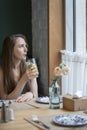 Young woman in cafe drinks lemonade from glass through straw. Girl sits at table in coffee shop and looks out the window Royalty Free Stock Photo