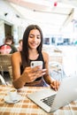 Young woman in a cafe reading a text message from her mobile phone. Latin female sitting at cafe table with laptop and using smart Royalty Free Stock Photo