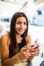 Young woman in a cafe reading a text message from her mobile phone. Latin female sitting at cafe table with laptop and using smart Royalty Free Stock Photo