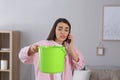 Young woman calling roof service while collecting leaking water from ceiling at home Royalty Free Stock Photo