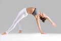 Young woman in Camatkarasana pose, grey studio background