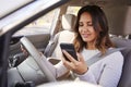Young woman in car checking her smartphone while driving Royalty Free Stock Photo