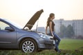 Young woman and a car with popped hood. Transportation, vehicles problems and breakdowns concept