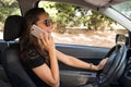 A smiling young woman in the car talks on the smart phone and drives