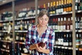 Young woman carefully reads the label on bottle while choosing wine in supermarket
