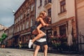 Young woman carrying her best friend on her back on city street. Happy teen girls laughing and having fun Royalty Free Stock Photo