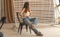 Young woman in casual clothes posing on chair in urban studio interior, teen girl in denim jeans sitting on black chair Royalty Free Stock Photo