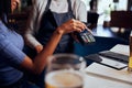 Young woman in casual clothing paying for dinner with card machine next to waitress Royalty Free Stock Photo