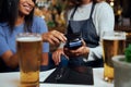 Young woman in casual clothing paying for dinner with wireless technology next to waitress Royalty Free Stock Photo