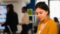 Young woman working at laptop sitting at desk in busy financial startup company