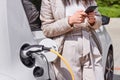 Young woman charging an electric car at public charging station and pays using a mobile phone. Innovative eco-friendly vehicle. Royalty Free Stock Photo