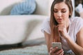 Young woman checking her smart phone lying on carpet Royalty Free Stock Photo