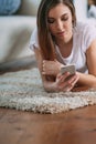 Young woman checking her smart phone lying on carpet Royalty Free Stock Photo